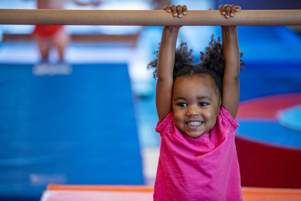 young girl hanging from a gymnastics bar