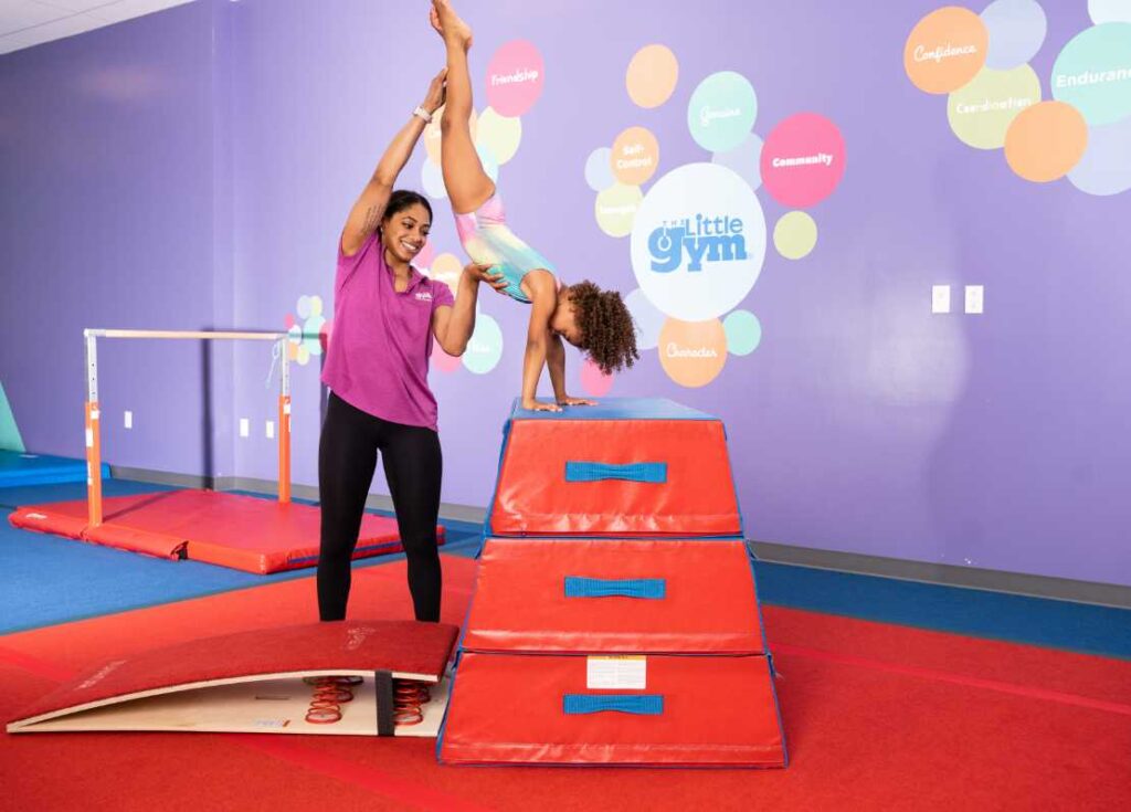 pre-k gymnastics instructor helping a young girl
