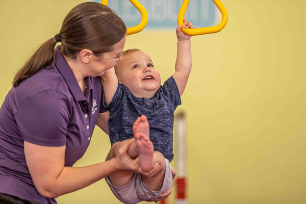 the little gym instructor supporting a toddler on gymnastics rings